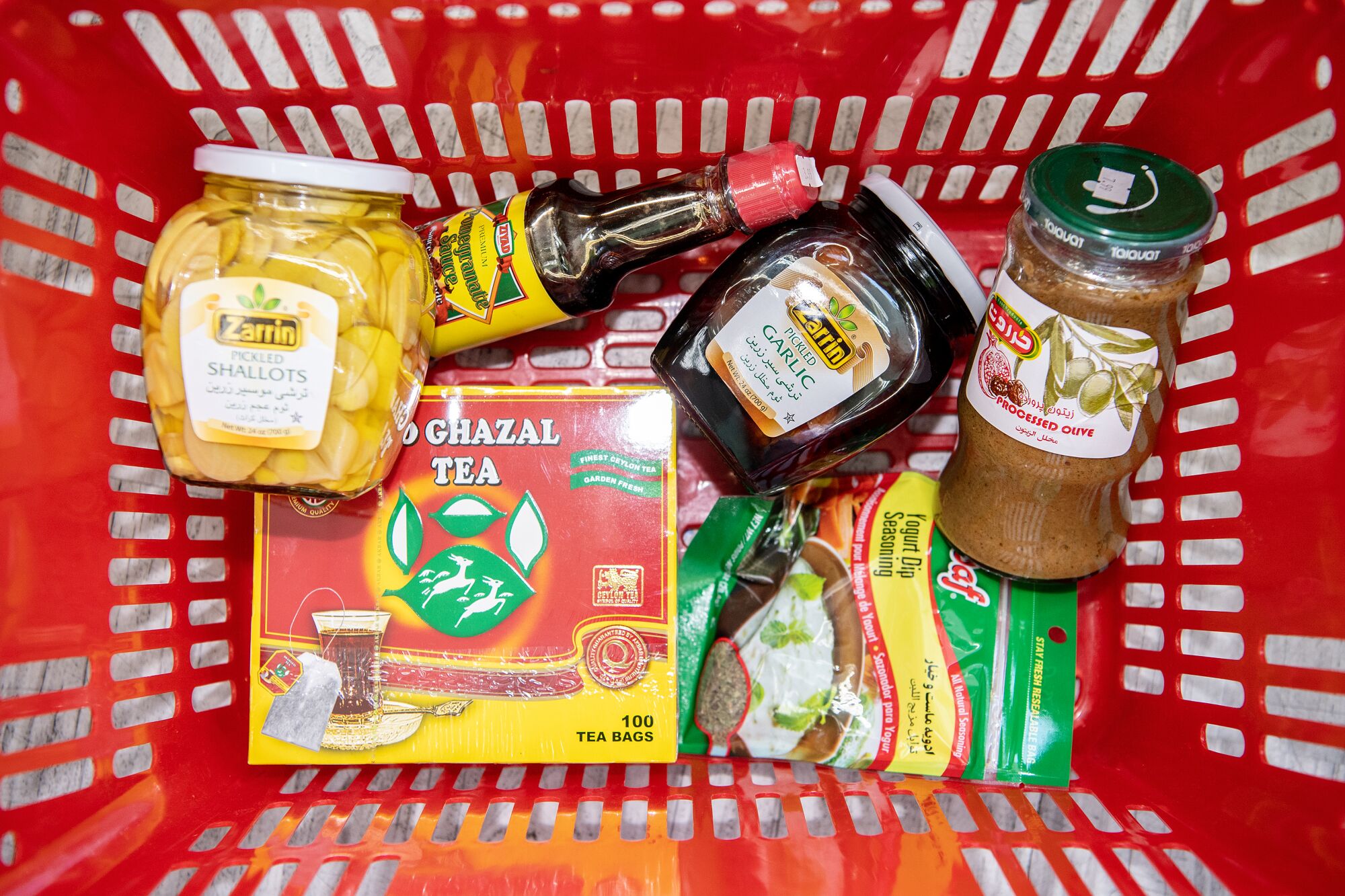Items in a red plastic shopping basket include tea, jams and bottled sauces.