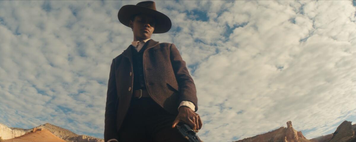 A person in a dark suit and dark hat looks down toward the ground, with a cloud-filled sky behind them