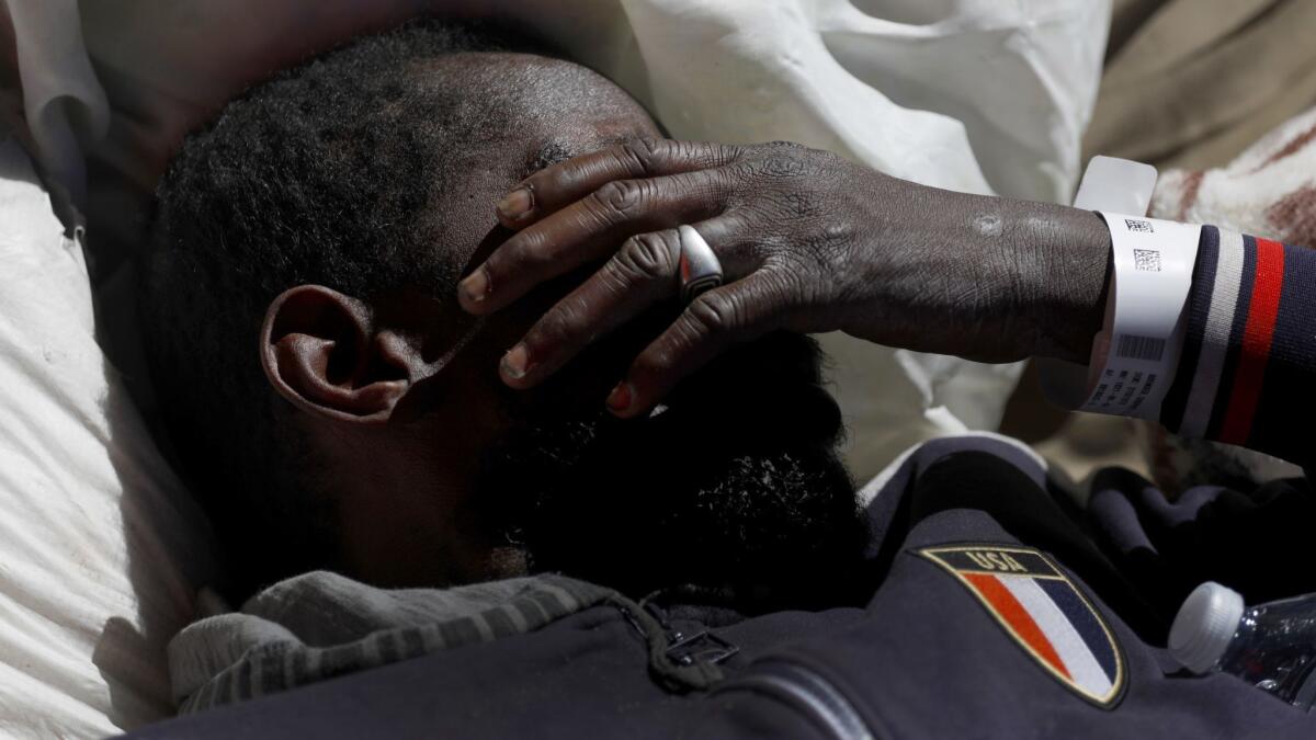 A man with a hospital bracelet on his wrist lies on a mattress on a sidewalk in South Los Angeles, refusing help from a Los Angeles Homeless Services Authority worker.