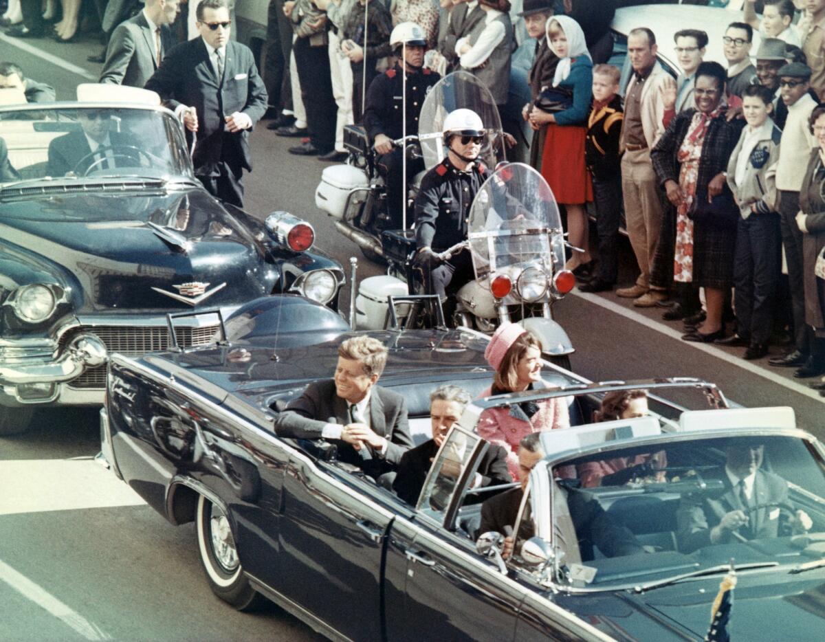 The president and first lady smile at the crowds lining their motorcade route in Dallas. Minutes later the president was assassinated as his car passed through Dealey Plaza.