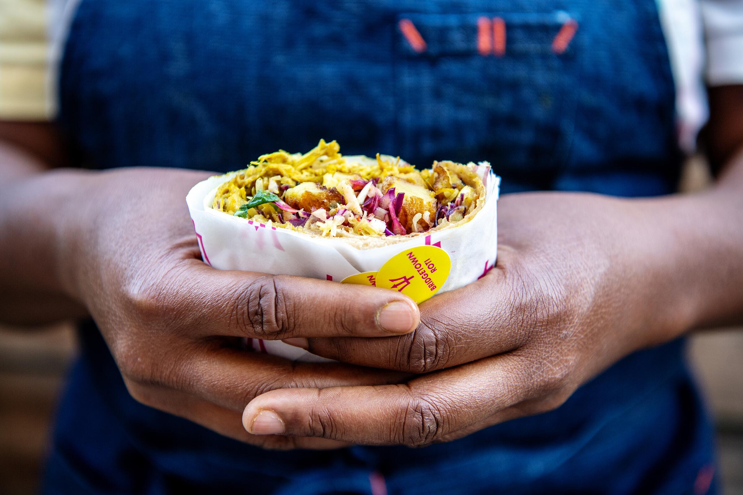 Rashida Holmes, chef and owner of the Bridgetown Roti pop-up, holds a roti wrap inside Crafted Kitchen in the Arts District. 