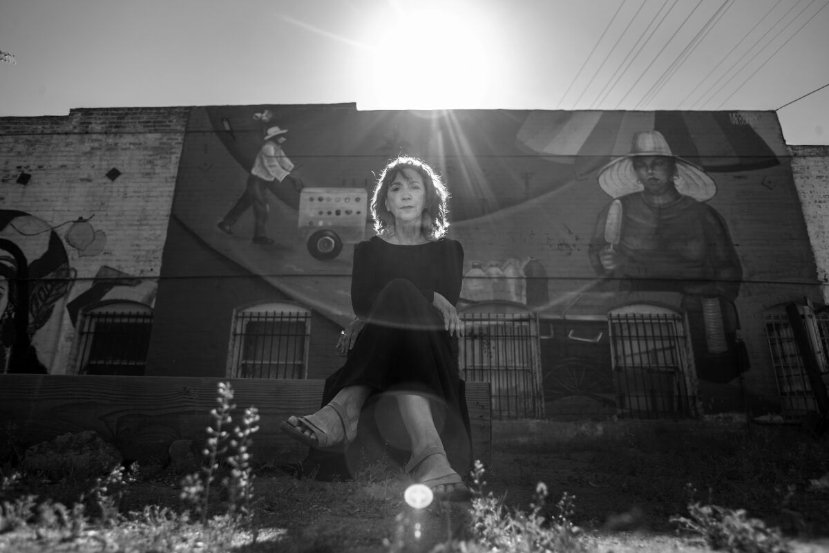 A black-and-white photo of a woman sitting in front of a building facade with a mural.