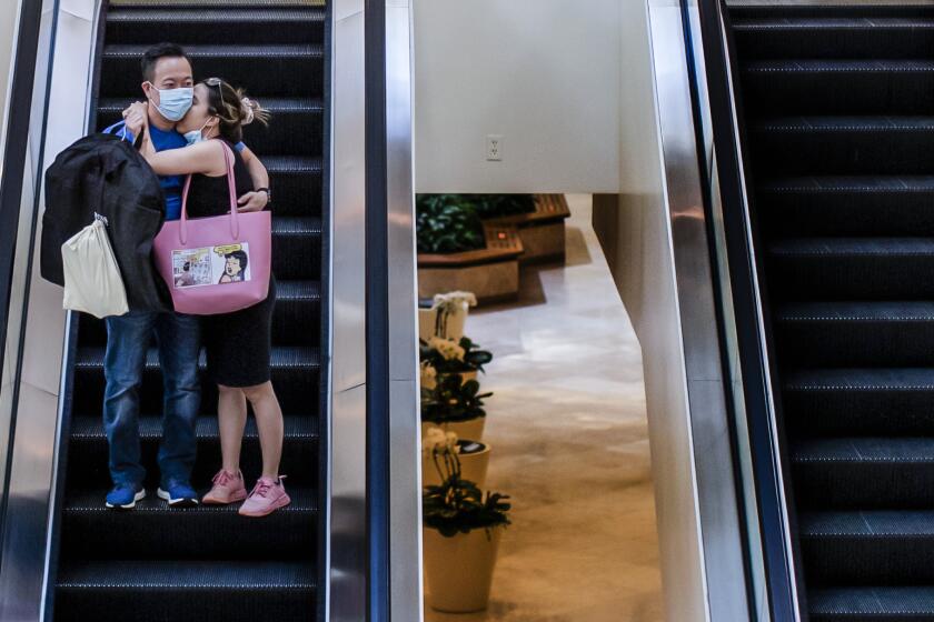 A masked couple embrace on the escalator while shopping at South Coast Plaza