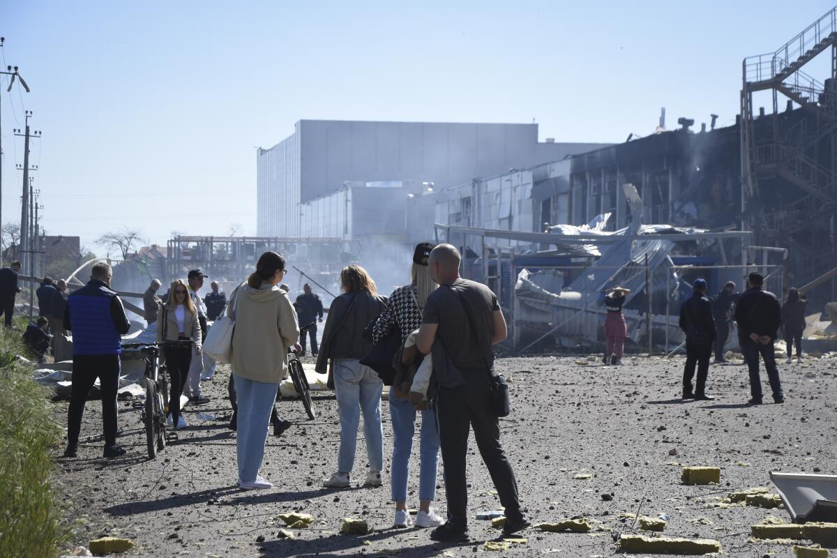 People stand near buildings damaged by Russian missiles.