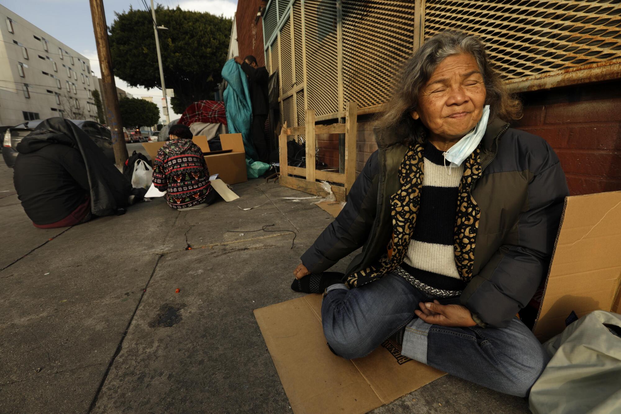 An older woman rests on a piece of cardboard that she uses to sleep on the sidewalk.