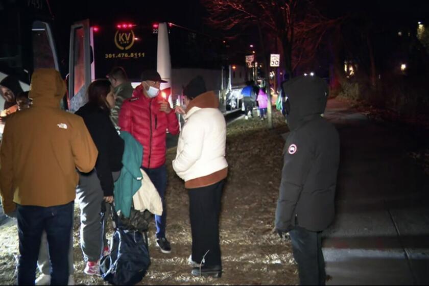 This image provided by WJLA shows migrant families as they get on to a bus to transport them from near the Vice President's residence to an area church after they arrived in Washington, Saturday, Dec. 24, 2022. Local organizers in Washington say three buses of recent migrant families arrived from Texas near the home in record-setting cold on Christmas Eve. Texas authorities have not confirmed their involvement. (WJLA via AP)