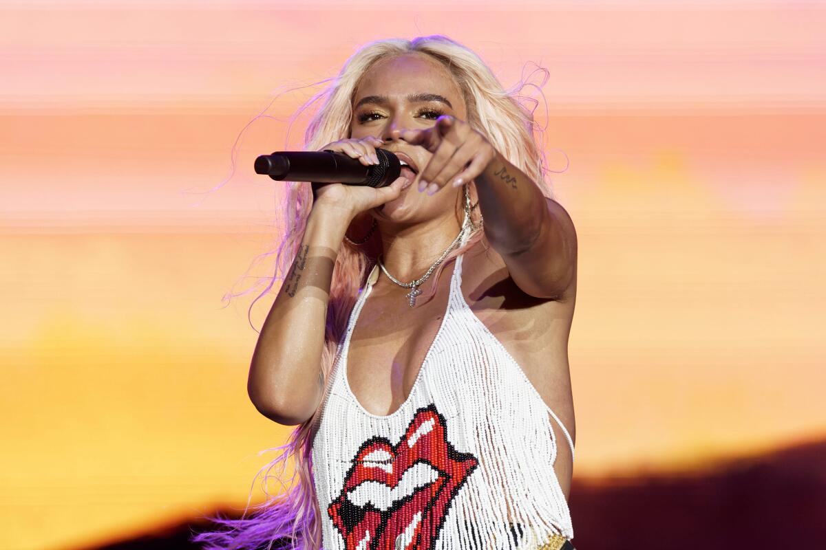 Karol G performs onstage in a cropped fringe top with a Rolling Stones logo