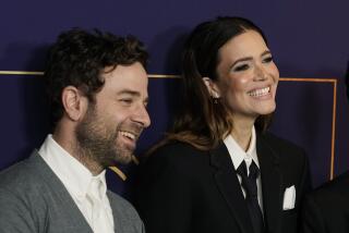 Mandy Moore, right, and her husband, songwriter Taylor Goldsmith, smile in suits on a red carpet