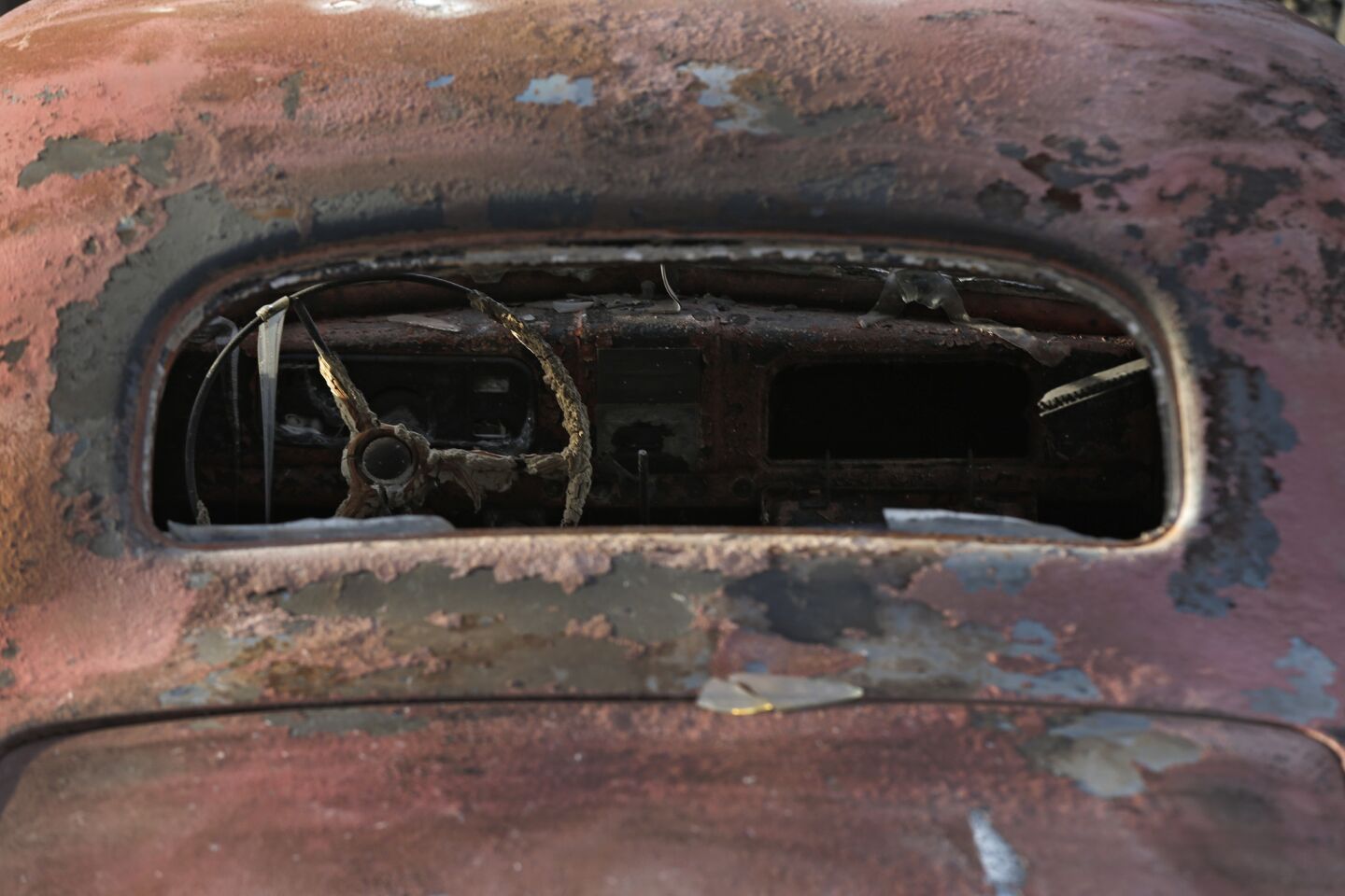 The melted ruins of an old car sits in the driveway of a home in the Angel Valley neighborhood of Weed, CA.