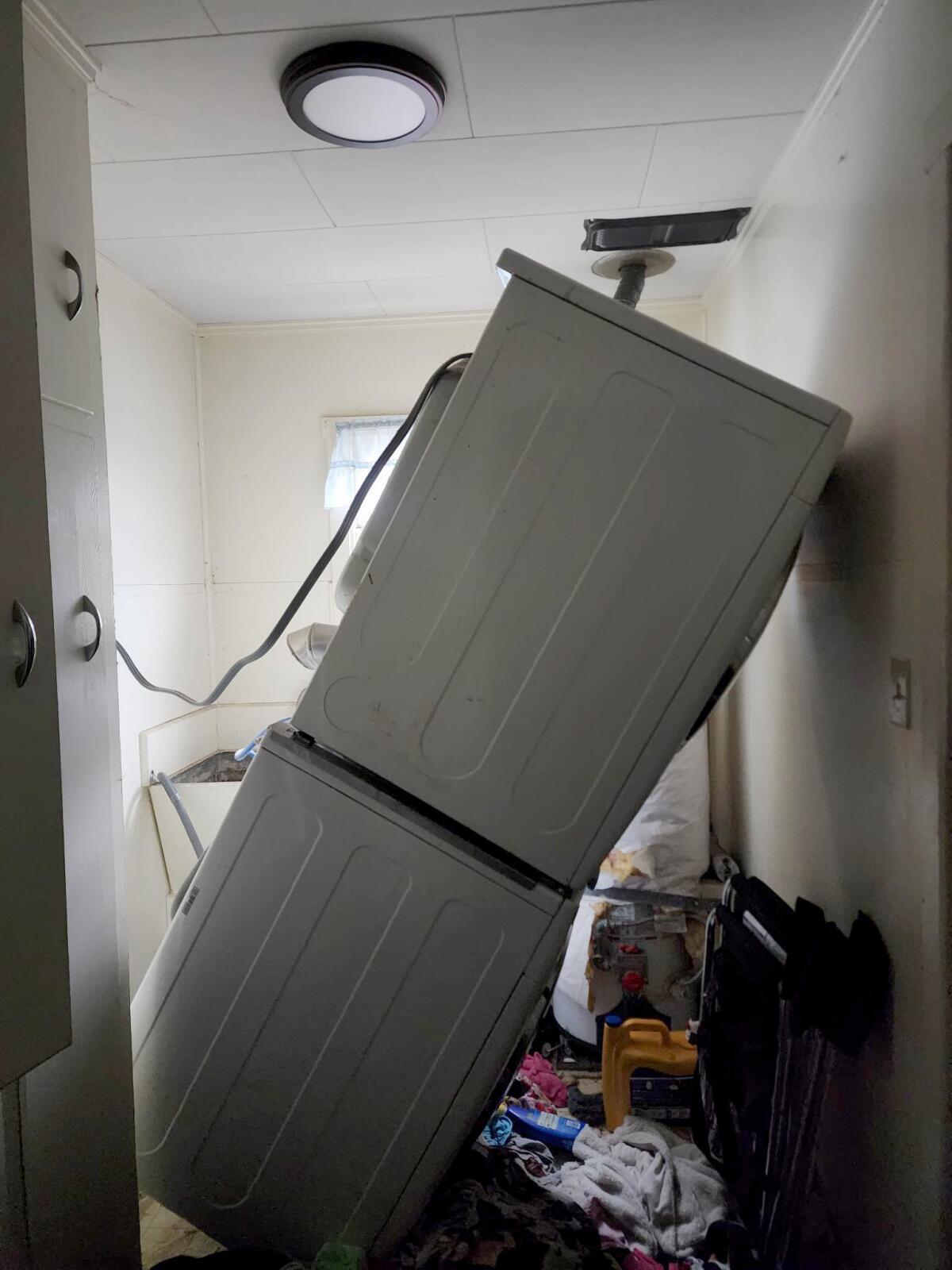 A stack of washing machine and a dryer is seen falling, leaning against a door with other items strewn about.