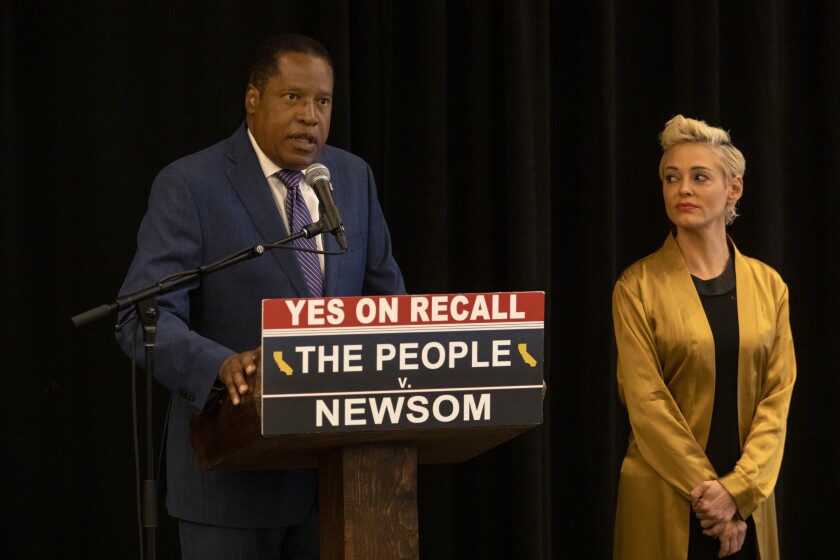 Larry Elder speaks at a podium next to Rose McGowan