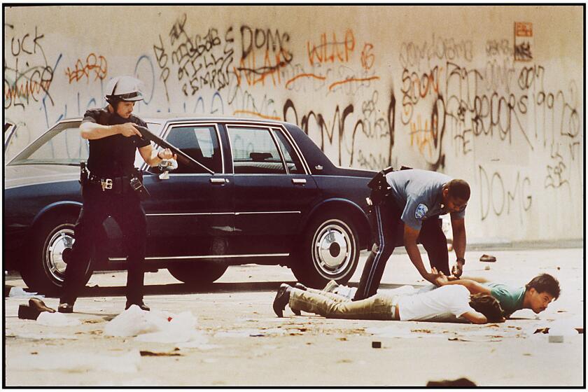 An LAPD officer trains his weapon on men arrested for looting as a State Police officer handciffs one of the suspects on 5/1/1992, on Martin Luther King Blvd. near Vermont Avenue.