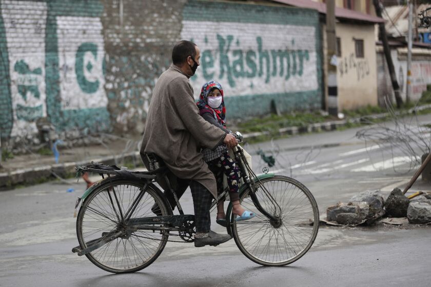 A Kashmiri man rides his bicycle carrying a girl wearing a protective mask during lockdown in Srinagar, Indian controlled Kashmir, Saturday, April 18, 2020. Indian Prime Minister Narendra Modi on Tuesday extended the world's largest coronavirus lockdown to head off the epidemic's peak, with officials racing to make up for lost time. (AP Photo/Mukhtar Khan)