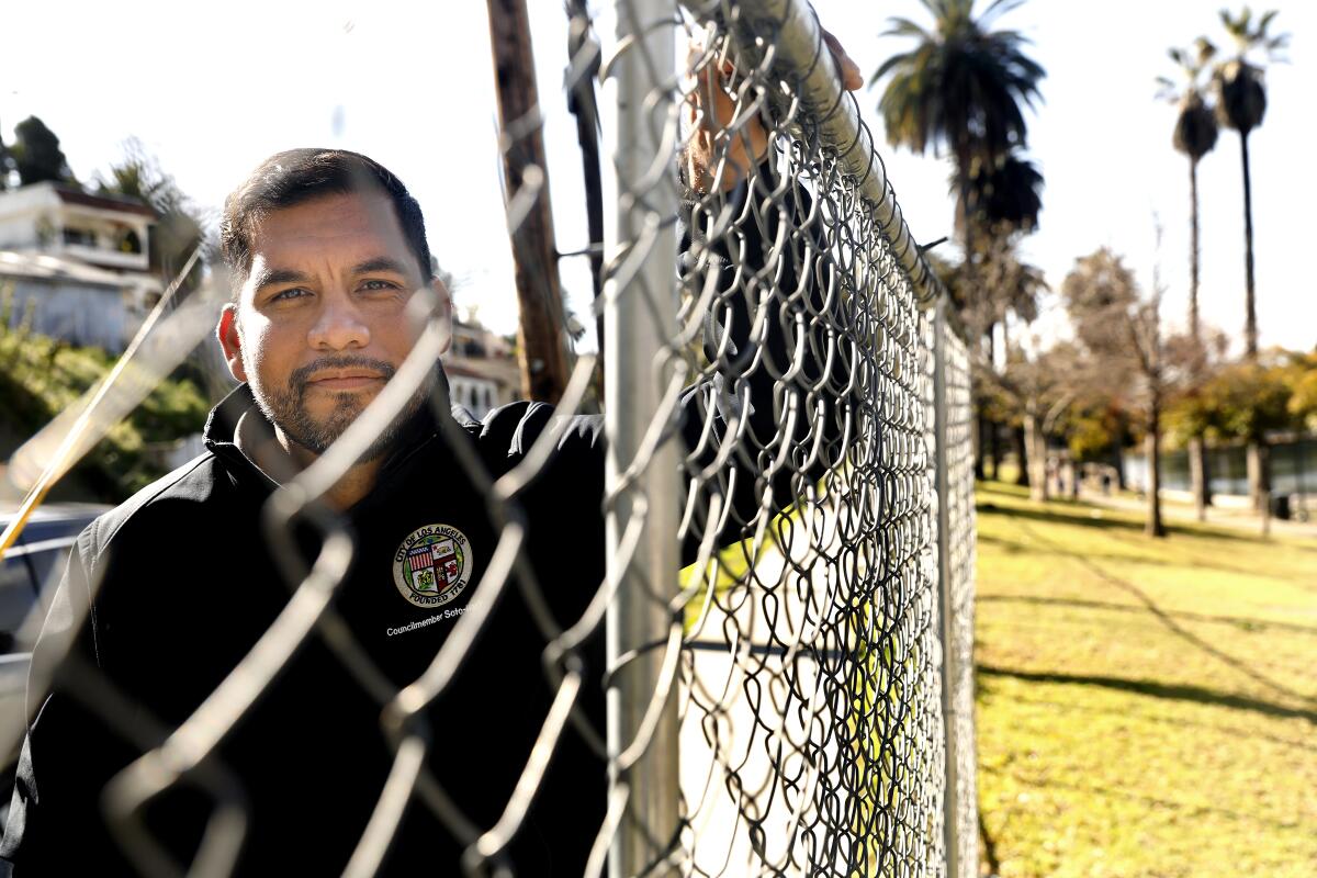 A man stands next to a chain-link fence running along a grassy area 