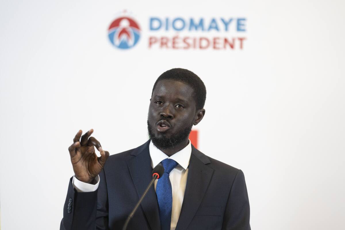 Bassirou Diomaye Faye speaks into a microphone in front of a background that reads "Diomaye President"