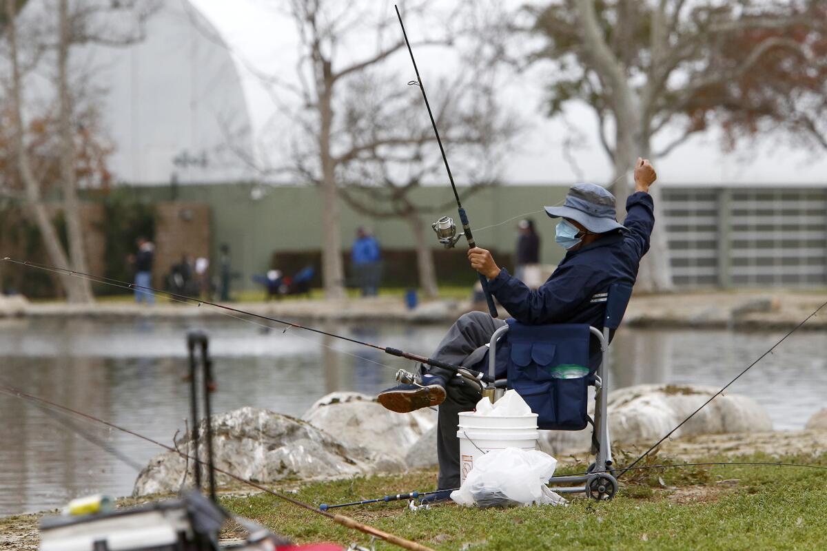 A fisherman wearing a face mask straightens his fishing line on Thursday at Mile Square Park in Fountain Valley.