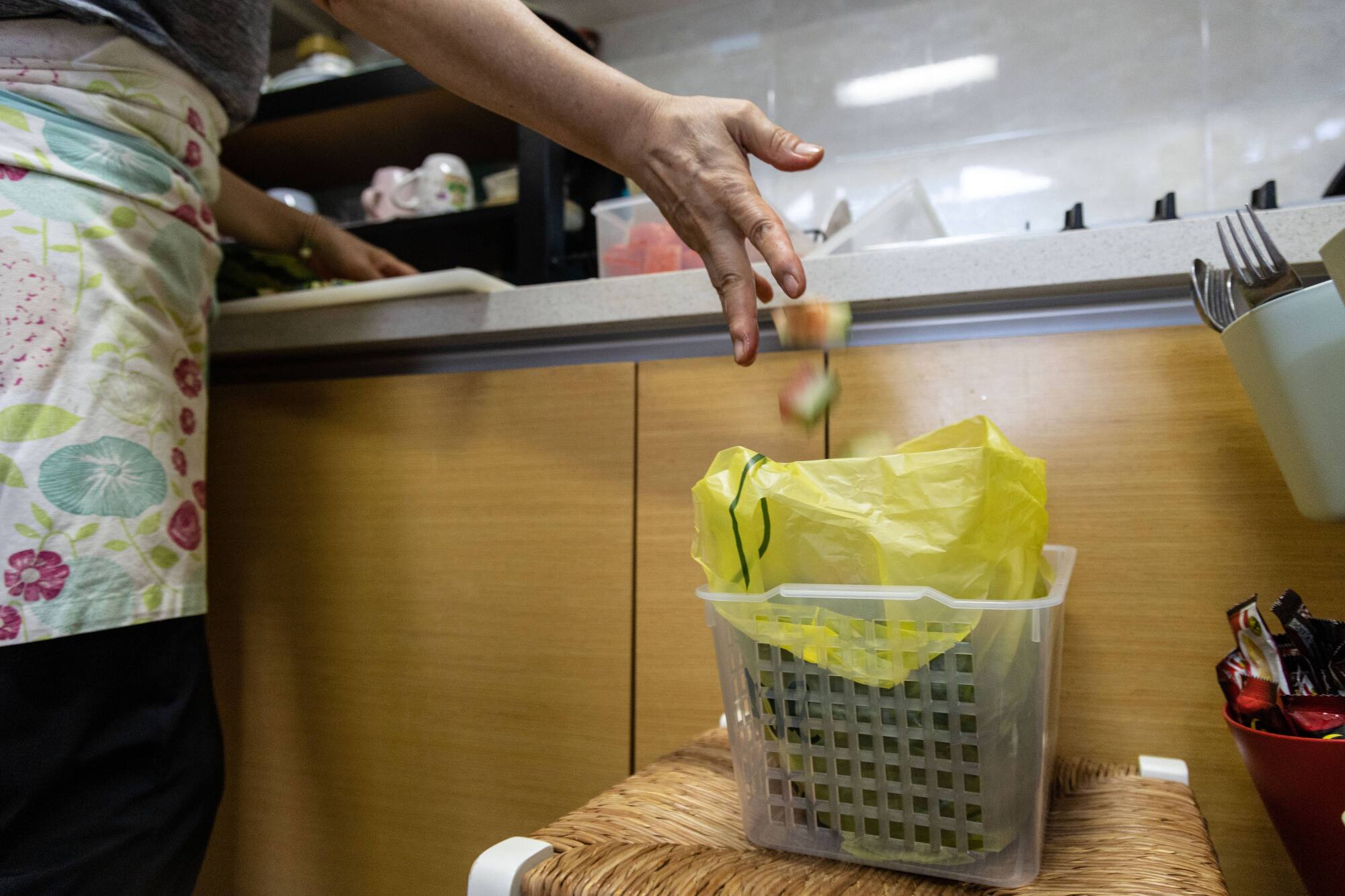 A woman disposes a waste from cutting a watermelon to a plastic bag designated for food waste at home.