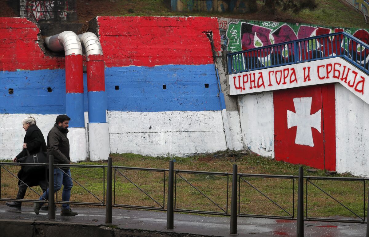 People walk by graffiti showing a Serbian flag, left, and text reading "Montenegro and Serbia'' in Belgrade, Serbia, Monday, Jan. 27, 2020. (AP Photo/Darko Vojinovic)