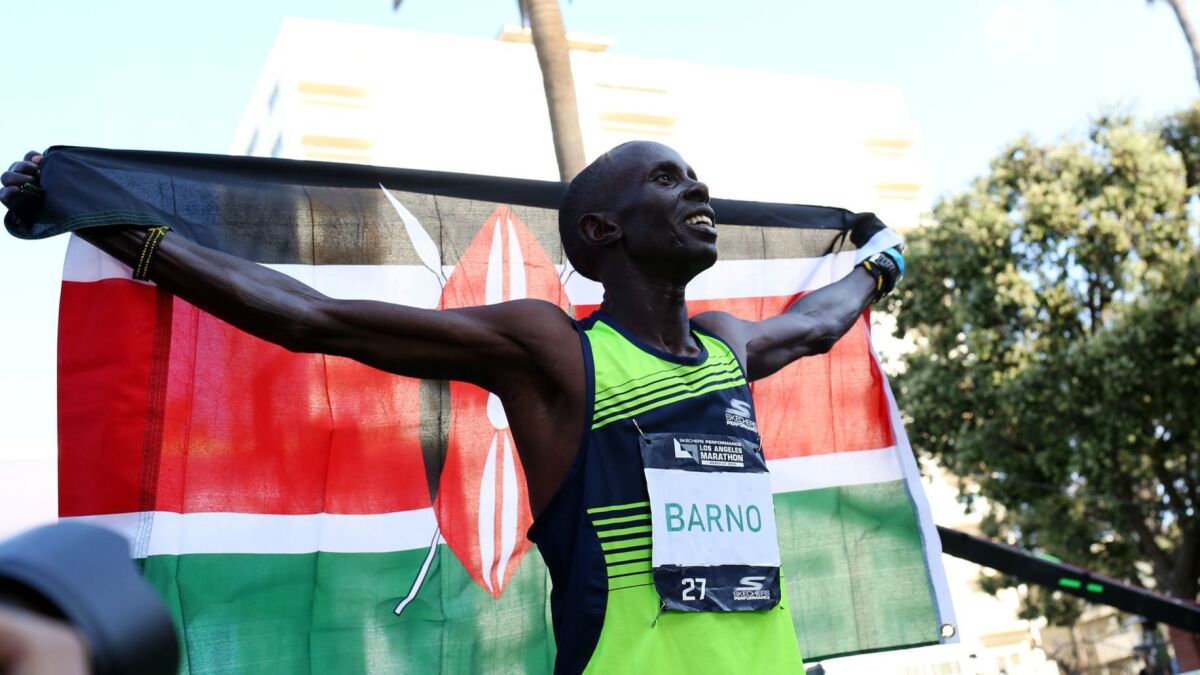 Elisha Barno celebrates with the flag of Kenya after winning the 34th running of the Los Angeles Marathon on Sunday.