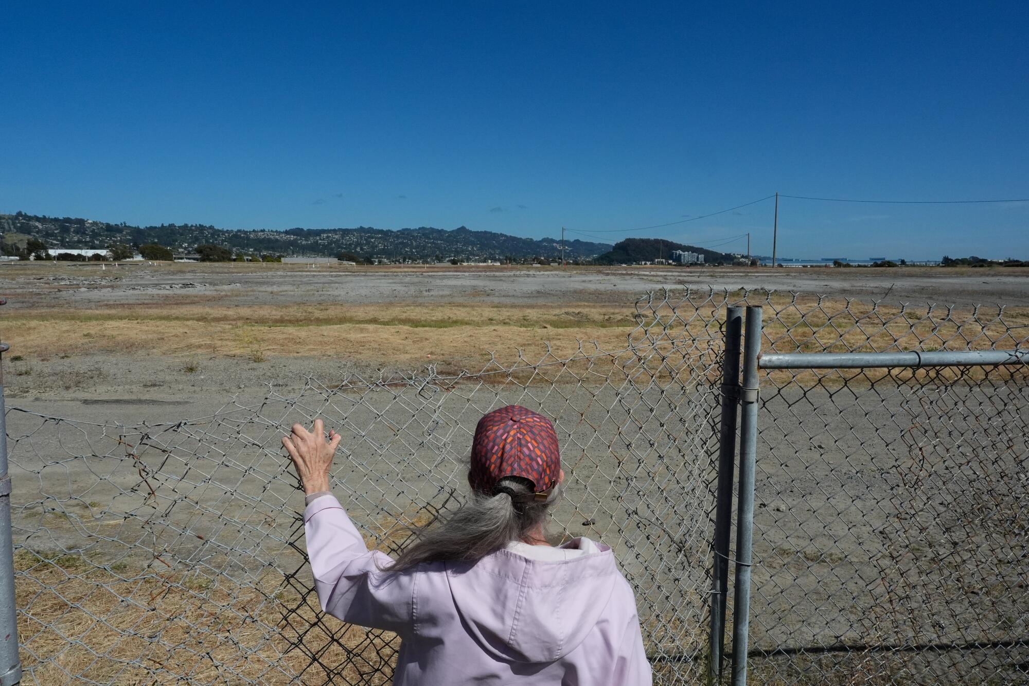 A woman looks at a field through a chain-link fence.