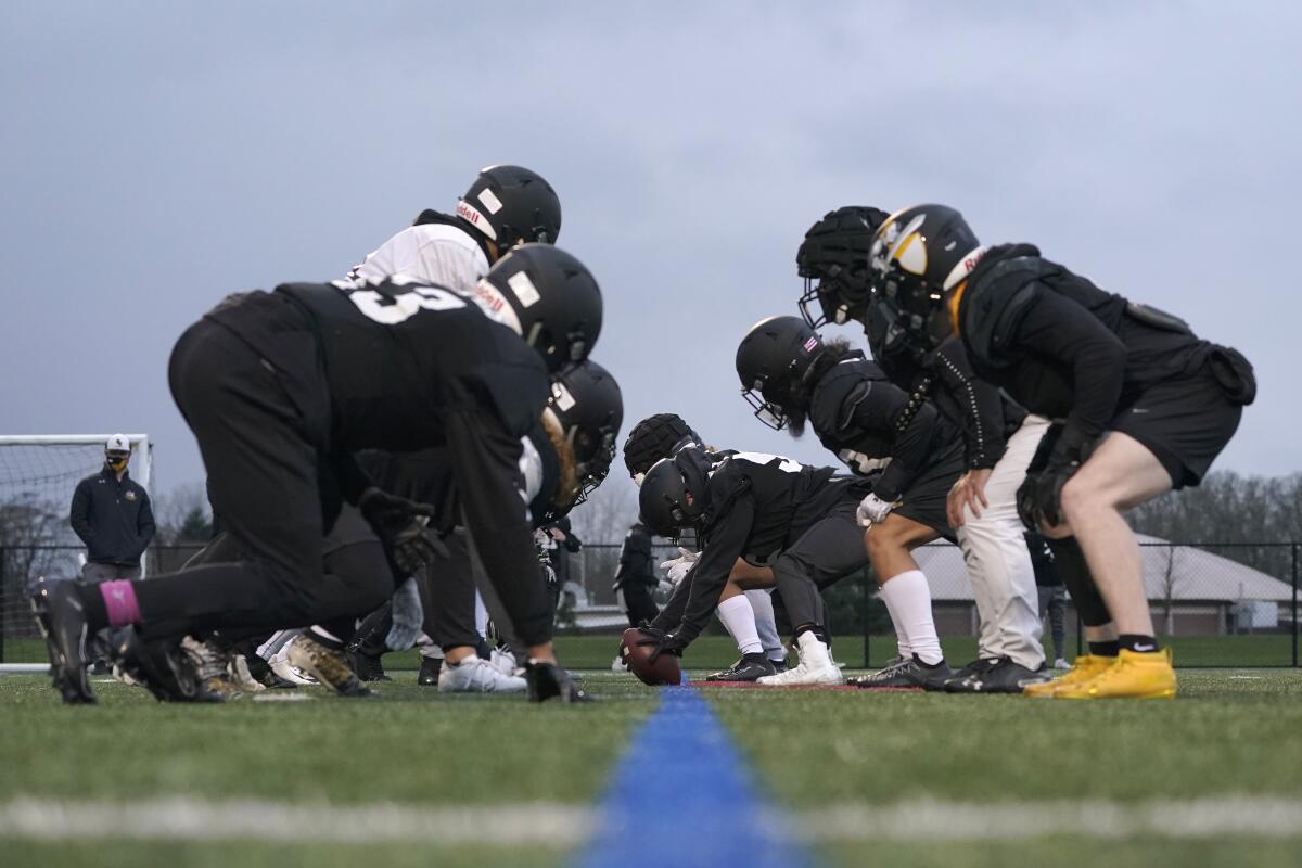 College football players wait for the snap on the line of scrimmage during practice.