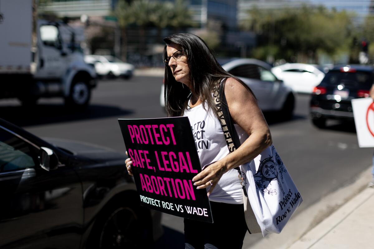 A woman alongside a busy street holds a sign that says, "Protect safe, legal abortion"