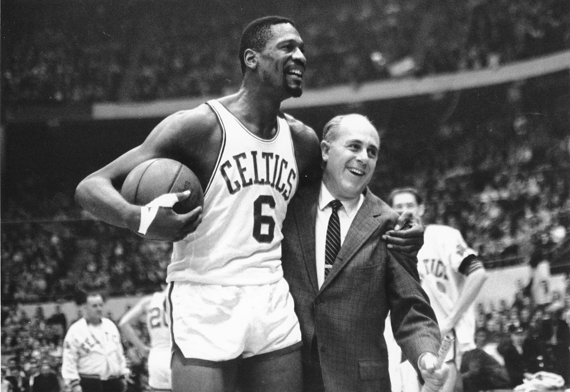 Bill Russell puts one arm around coach Red Auerbach and holds a basketball in the other arm