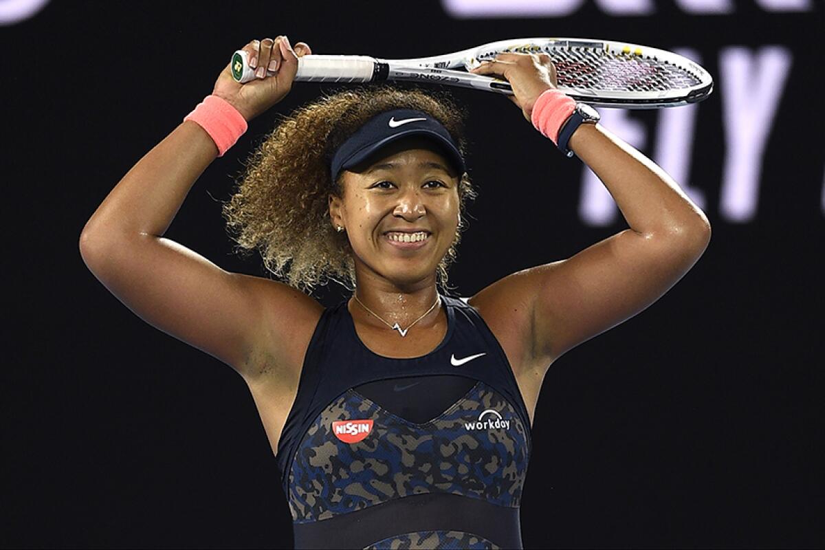 Naomi Osaka in tennis gear with a racket over her head.