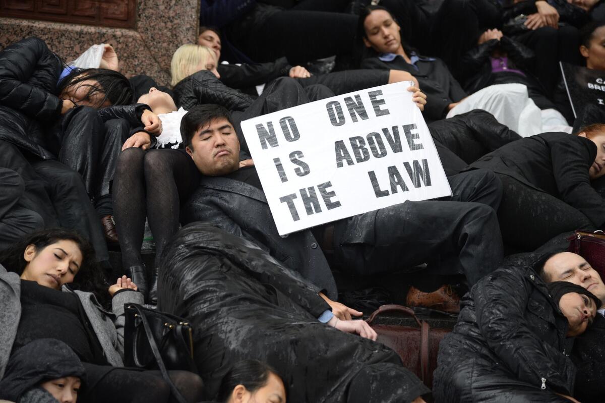 Lawyers, law students and others lie on the ground in the rain outside an L.A. courthouse to protest the handling of killings by police.