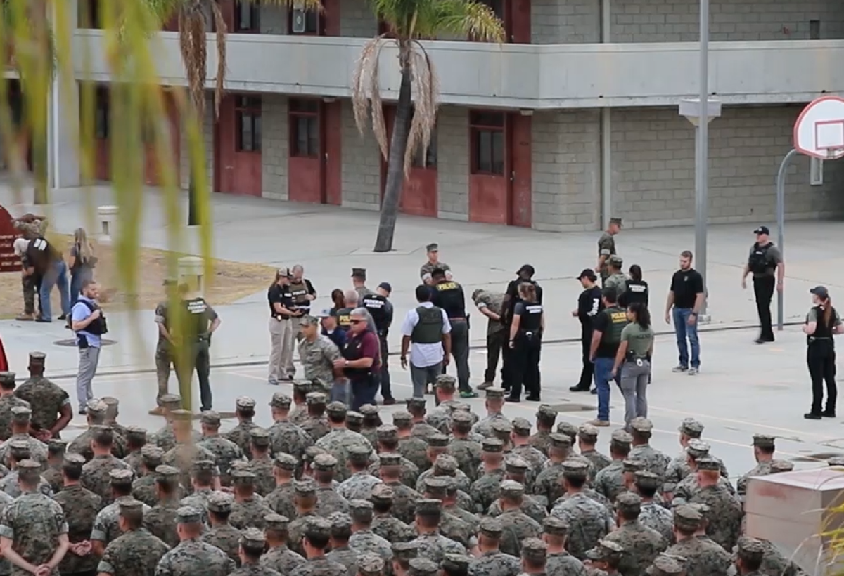 Military law enforcement, including NCIS, handcuff, search and walk detained Marines in front of their peers at Marine Corps Base Camp Pendleton in July.