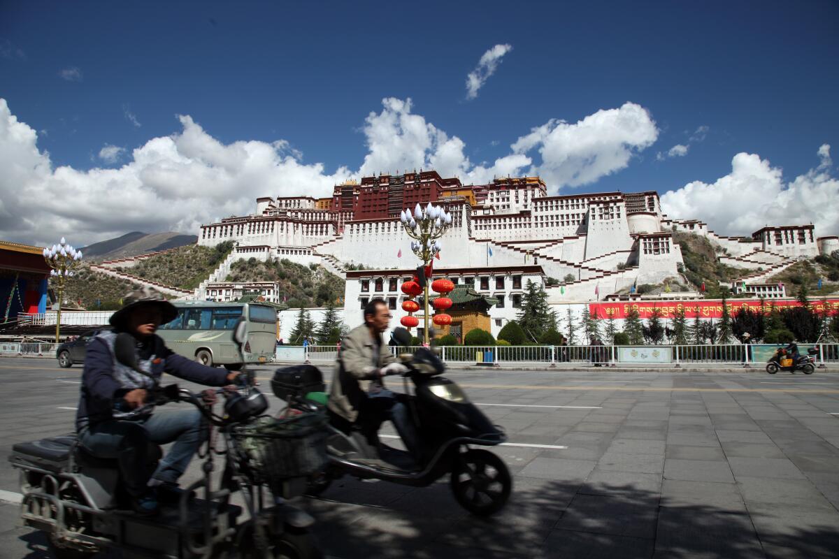 People on scooters riding past Potala Palace in Lhasa