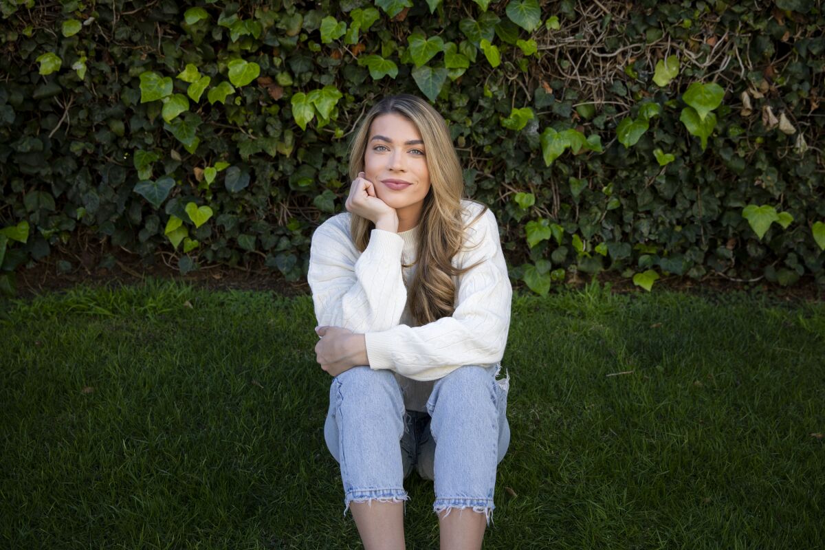 a woman wearing jeans and a white shirt sits in the grass