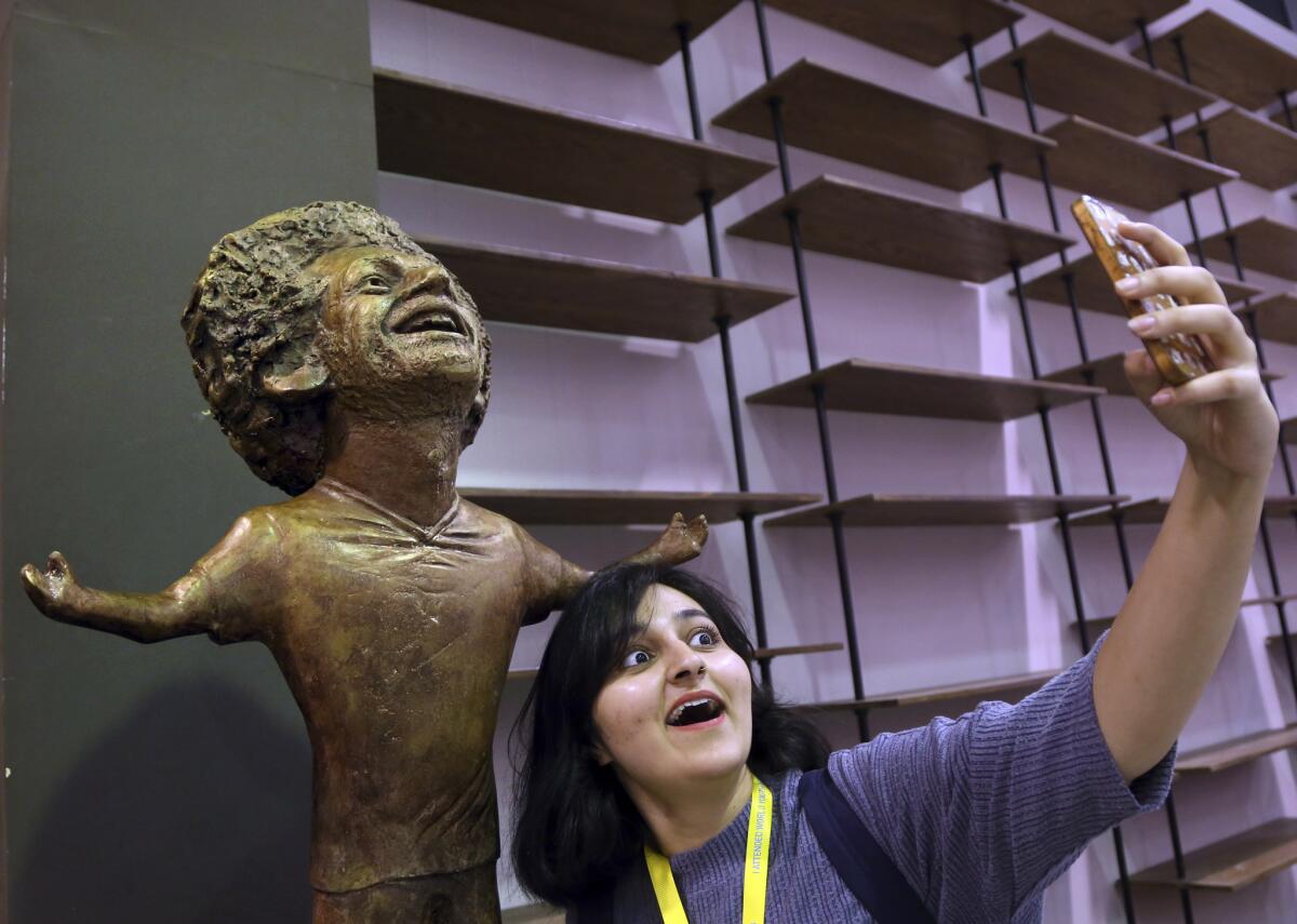 A participant at an international youths gathering poses for selfie with a bronze statue of Liverpool striker Mohammed Salah in a conference hall, in Sharm El Sheikh, Egypt, Monday, Nov. 5, 2018. The statue unveiled in his native Egypt has kicked up a social media storm because of its poor resemblance. It depicts Salah with a disproportionately large head and baby arms stretched in the celebratory pose the 26-year-old Egyptian took in the latter part of last season after scoring goals.