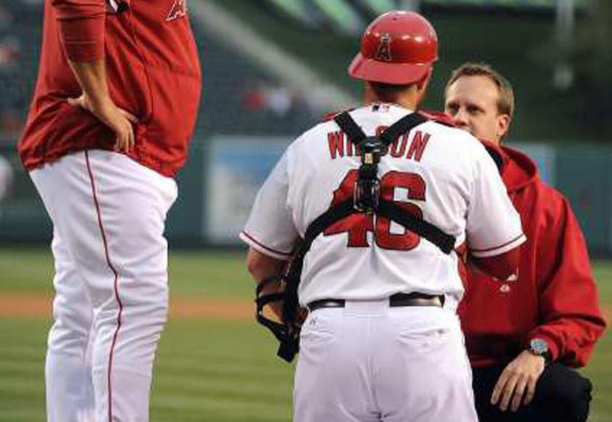 An Angels trainer examines catcher Bobby Wilson after he was injured Monday night.