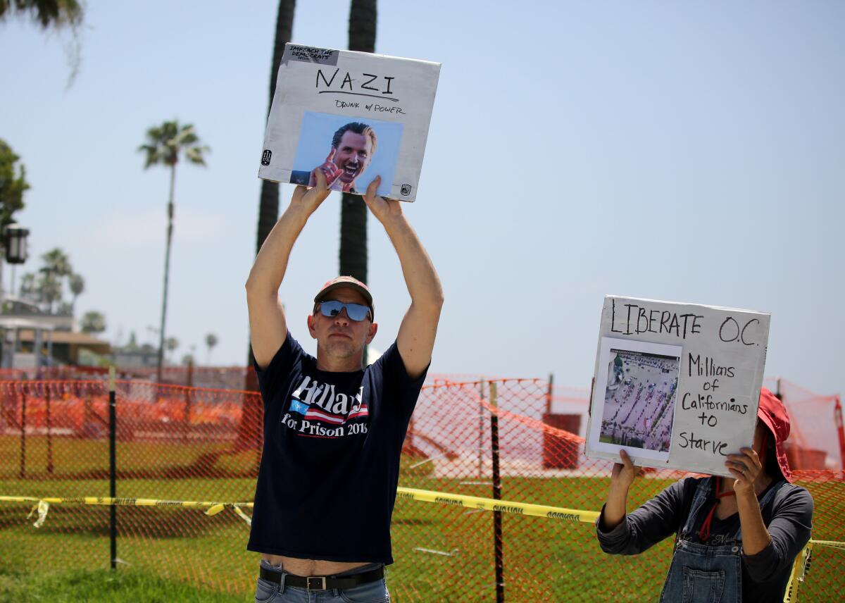 Protesters hold up signs next to the fenced-off Main Beach Park in Laguna Beach on Saturday.