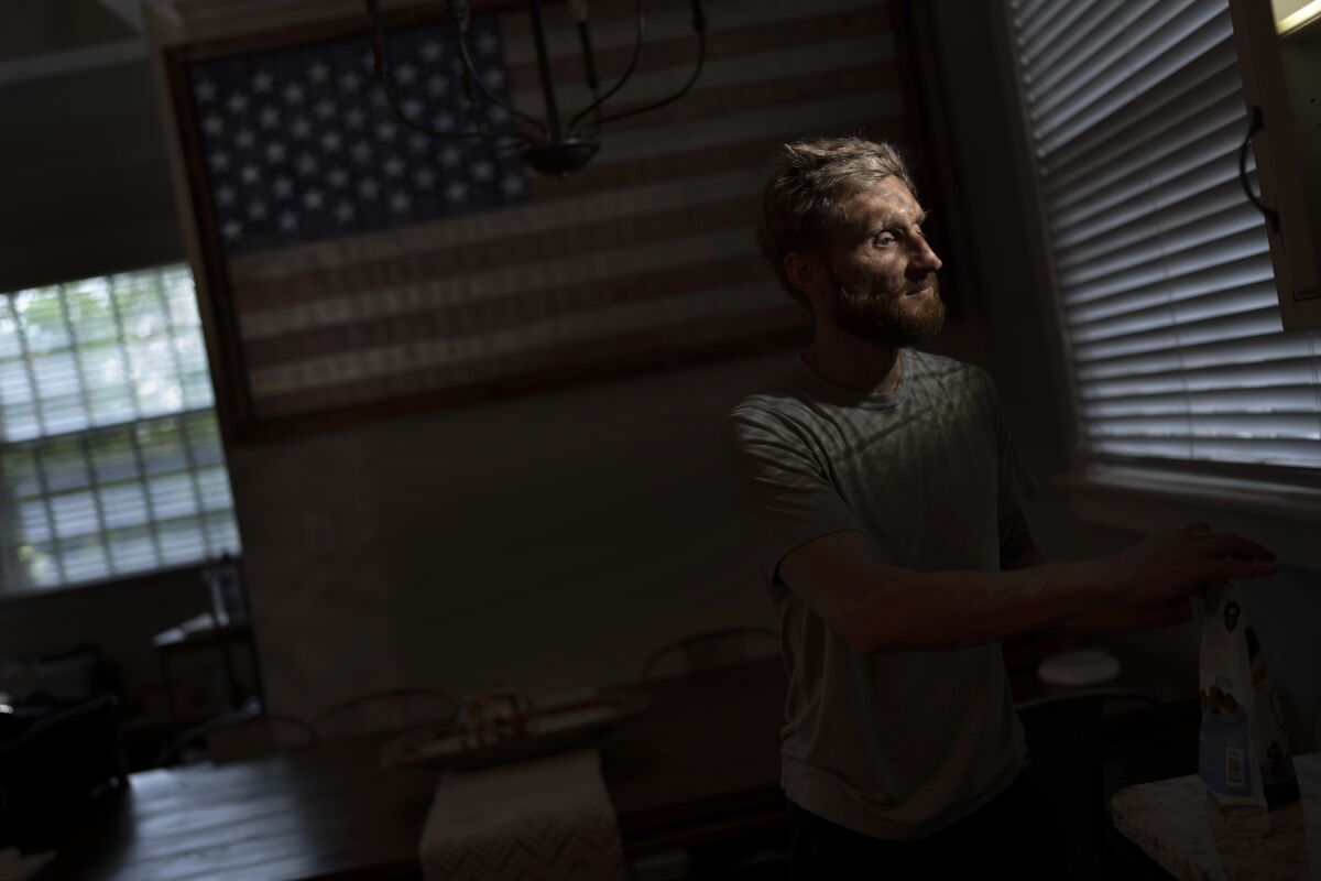 Brad Snyder prepares tea for his wife in their kitchen decorated with a flag handcrafted by Brooklyn firefighters using recycled firehose, in Princeton, N.J., on Wednesday, Aug. 4, 2021. Losing his sight, he says, seems to matter more to other people. (AP Photo/Emilio Morenatti)