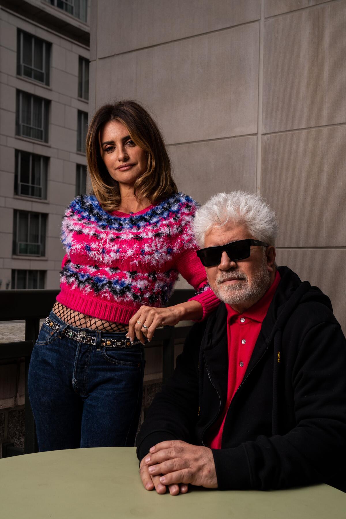 Penelope Cruz stands with her arm resting on the seated director Pedro Almodovar's shoulder.