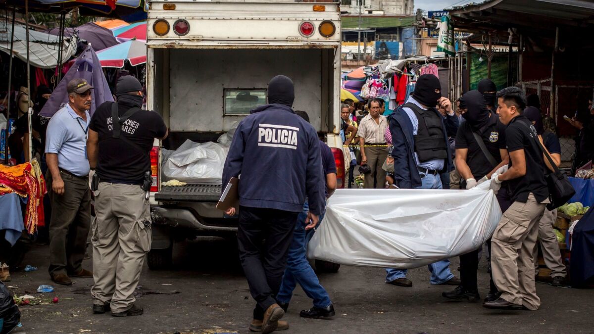 Police investigators carry a body to a forensic vehicle, after a shootout between private security guards and gang members, at the central market in San Salvador, El Salvador on March 15, 2017.