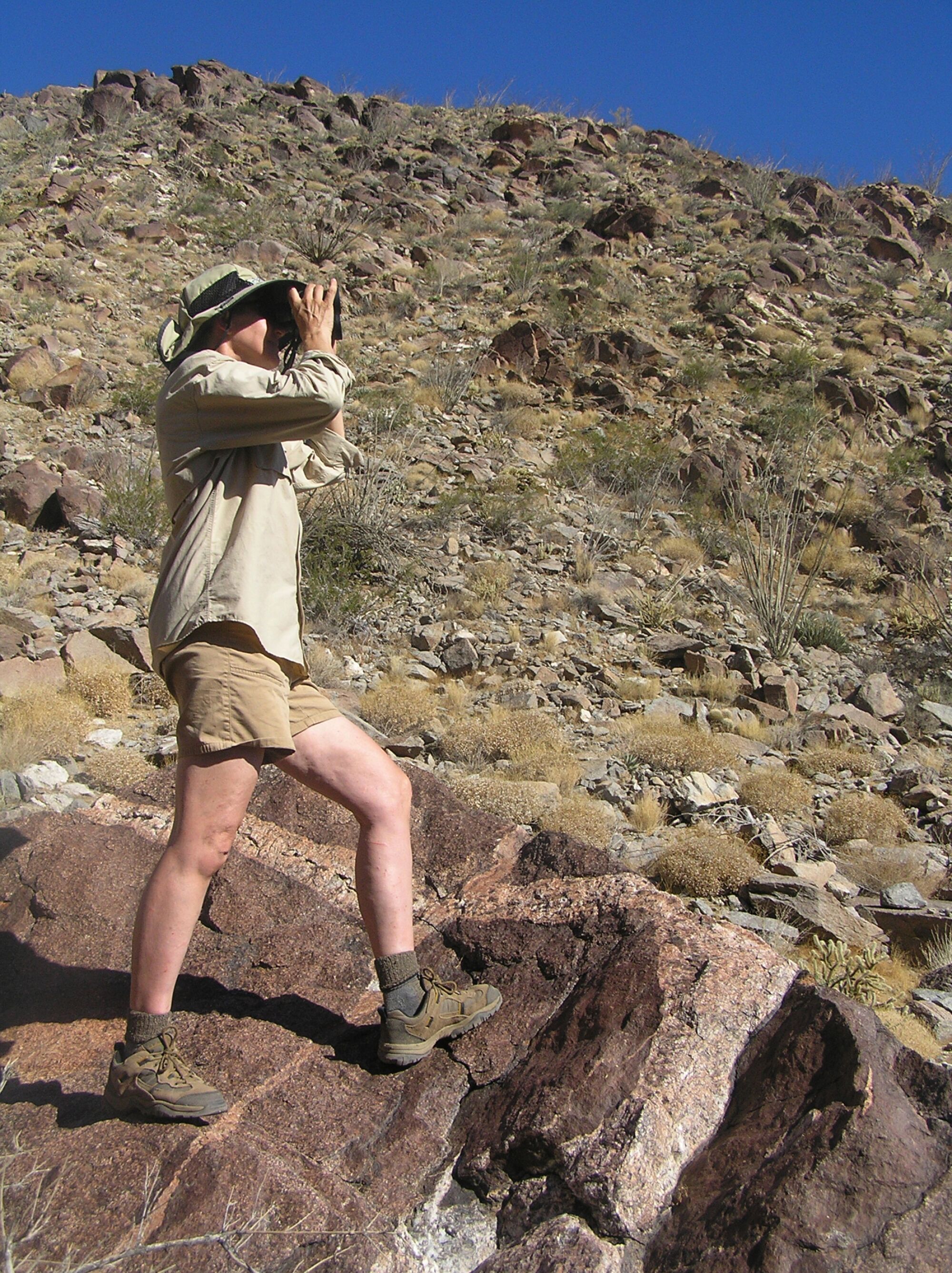 Callie Mack looks through binoculars while standing on a rock.