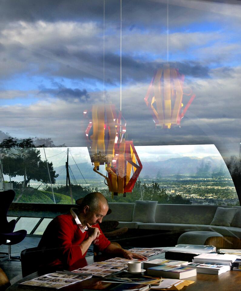 Publisher Benedikt Taschen, photographed at work in the home in 2005, sits behind expanses of glass reflecting clouds and sky.