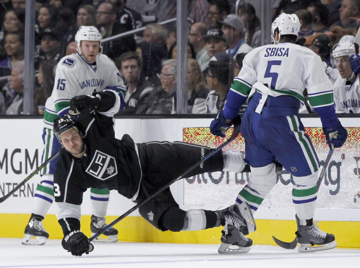 Kings' Kyle Clifford gets knocked to the ice by Vancouver's Luca Sbisa, right, with Derek Dorsett watching on Tuesday night.