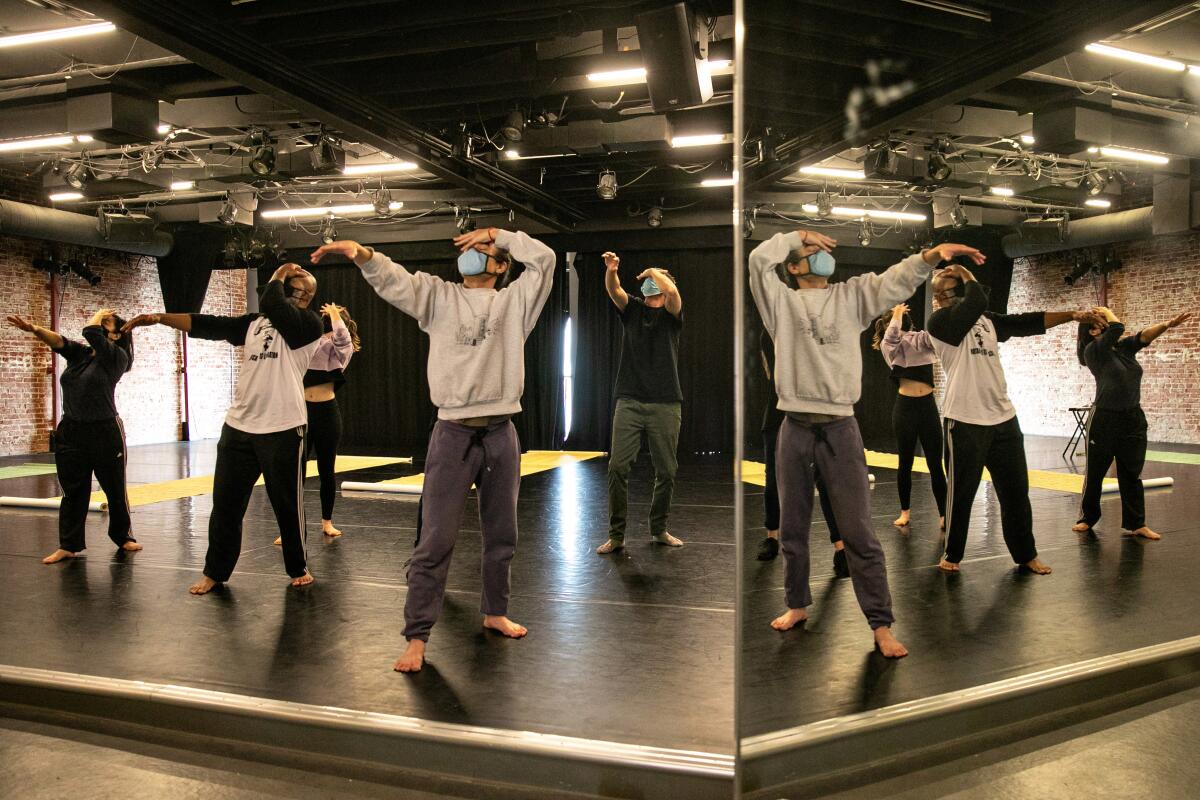 Five dancers in sweats rehearse in a studio.