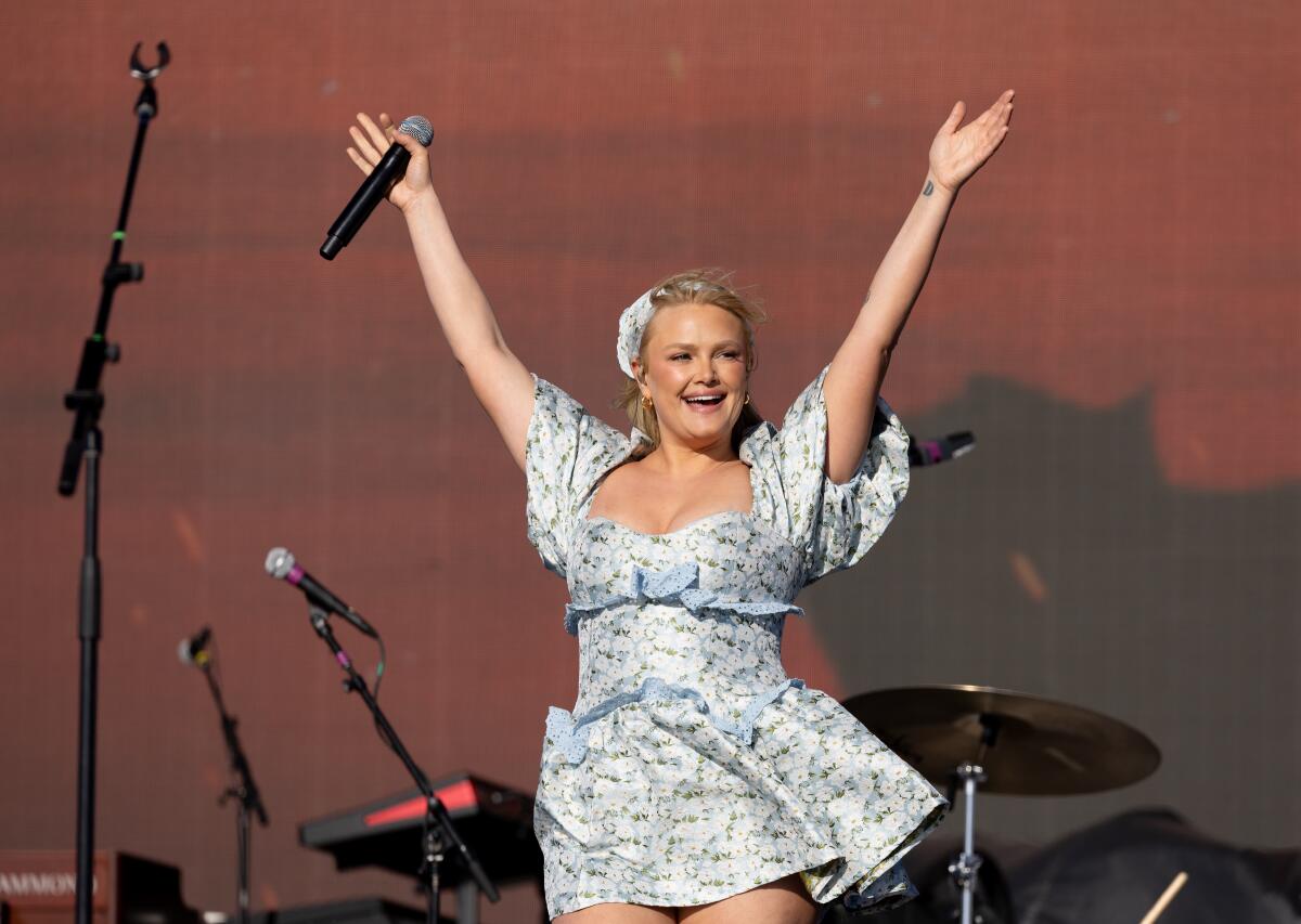 A woman with a microphone raises her arms.