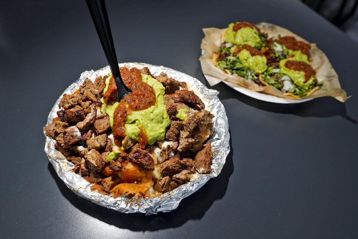 Two plates, one covered in foil with meat and a plastic fork sticking out, and one with tacos on it