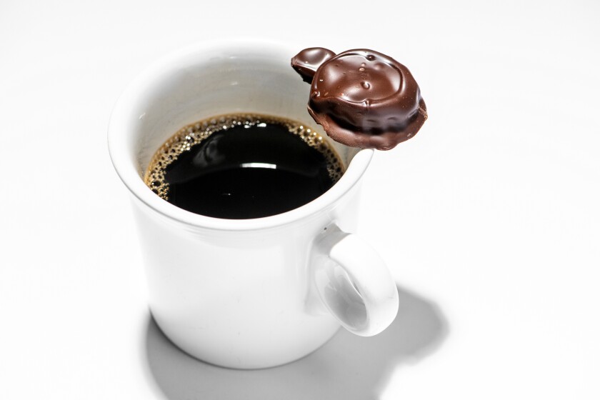 A See's Candies Scotch Kiss rests on a mug filled with coffee. 