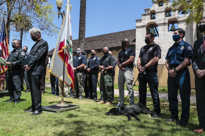 Law enforcement officers stand in a grassy courtyard next to U.S. and California flags.