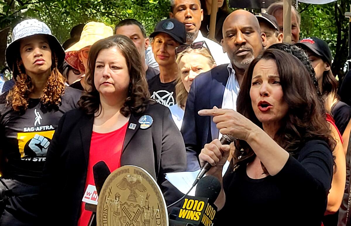 SAG-AFTRA president Fran Drescher stands outdoors among a crowd of actors, speaking into a microphone