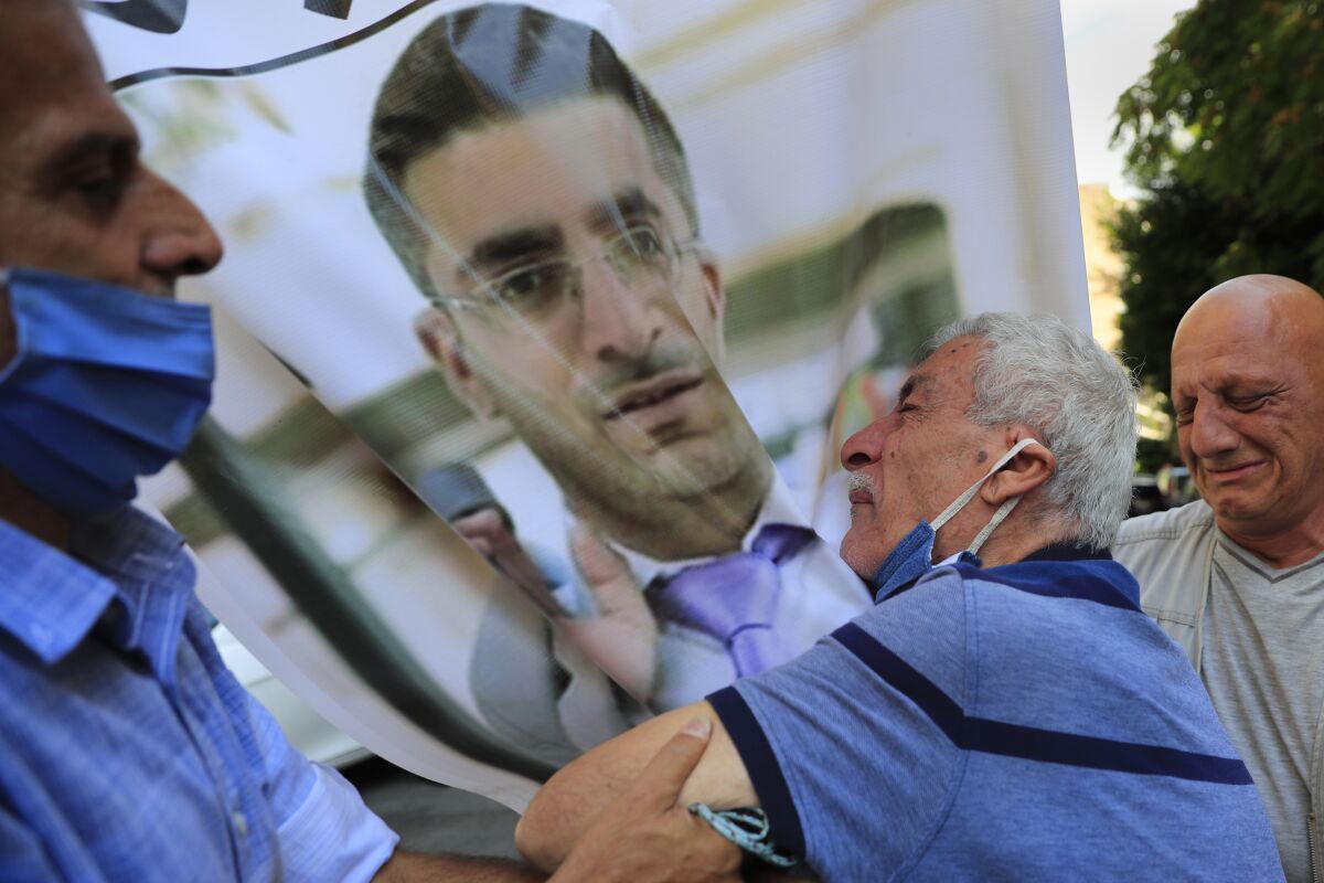 A white-haired man holds a large image of a younger man