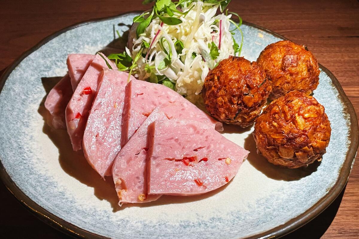 Budonoki's naem, pink triangles of house-made pork sausage, next to fried rice balls and a mound of slaw on a white plate