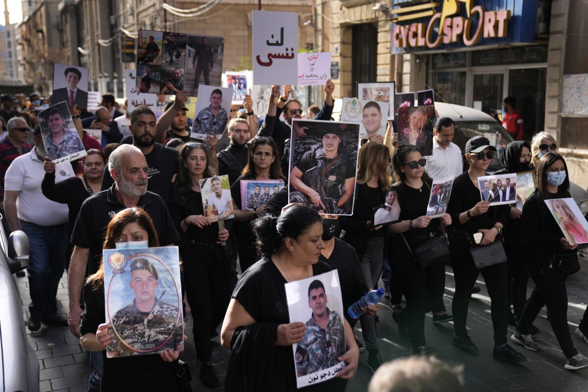 Relatives of victims of the August 4, 2020 Beirut port explosion hold portraits of their loved ones who died in the explosion, as they march during a gathering to mark twenty months since the blast that killed more than 200 people and injured thousands, in downtown Beirut, Lebanon, Monday, April 4, 2022. The Arabic placard reads:"Will not forget." (AP Photo/Hussein Malla)
